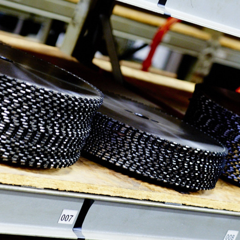 Närbild av flera slipskivor på en trähylla i ett förvaringsområde. Hjulen har en texturerad, mörk yta och är staplade horisontellt. Etiketter med siffror syns på hyllorna.