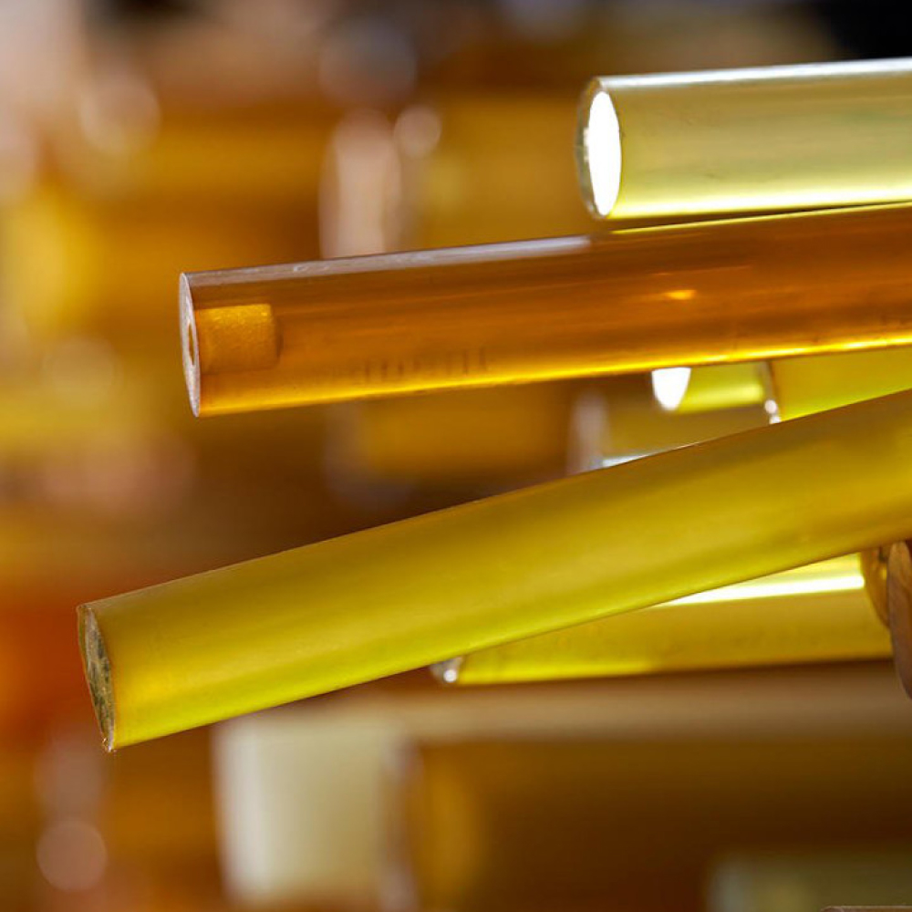 Närbild av genomskinlig bärnsten och gula stavar i olika längder och tjocklekar, anordnade horisontellt. De är släta och glansiga, reflekterar ljus och kastar subtila skuggor på varandra. Bakgrunden är suddig, fokuserar uppmärksamheten på stavarna.