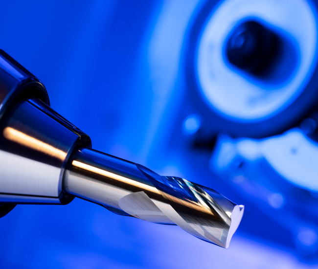 En närbild av en glänsande metallborr med en suddig blå bakgrund. Borrkronan är monterad och reflekterar belysningen och framhäver dess skarpa skäreggar och polerade yta.
